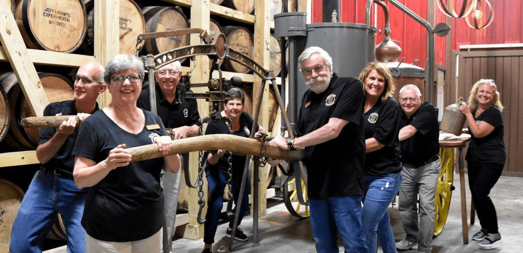 Distillery staff gathered around an antique barrel lift beside the racks